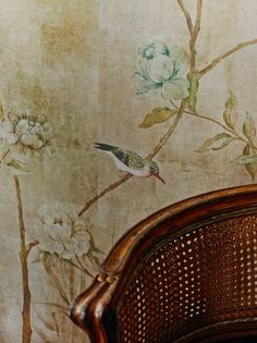 a bird sitting on top of a wooden chair next to a wall with flowers painted on it