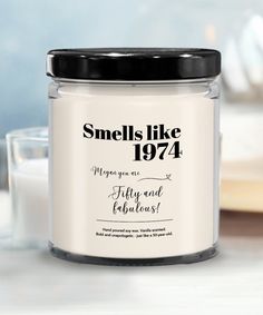 a candle that is sitting on a table next to a glass jar with the words smells like 1974 written in it