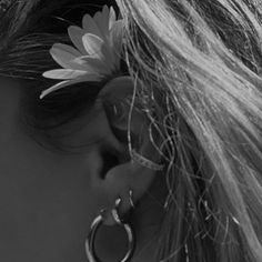 a woman with long hair wearing large hoop earrings and a flower in the middle of her ear