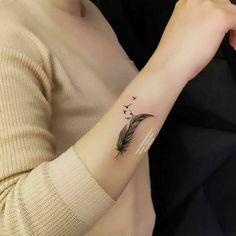 a woman's arm with a small feather tattoo on the left side of her arm