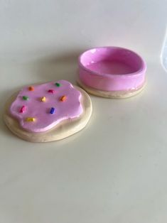 two decorated cookies with pink icing and sprinkles next to a bowl