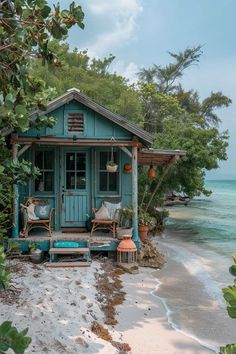 a small blue house sitting on top of a sandy beach next to the ocean and trees