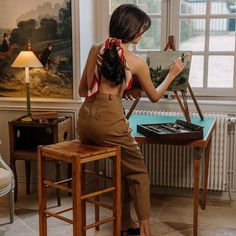 a woman sitting at a table with an easel and painting