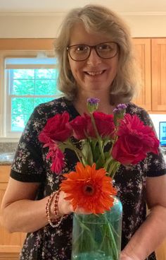 a woman holding a vase filled with red and pink flowers on top of a counter