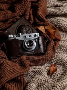 an old camera sitting on top of a blanket next to a brown object with leaves