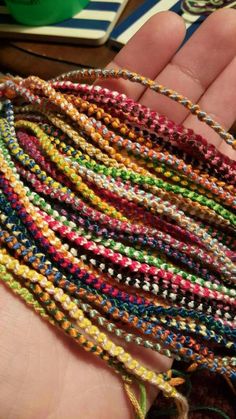 a person is holding several different colored beads in their hand and there are other bracelets on the table