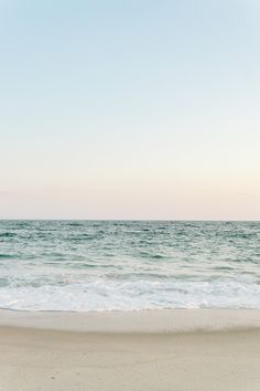 an empty beach with the ocean in the background