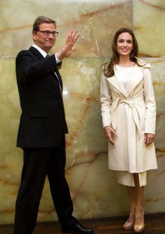 a man and woman standing next to each other in front of a large marble wall