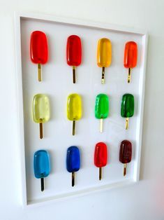 an assortment of colorful pops are displayed in a white shadow box on the wall,