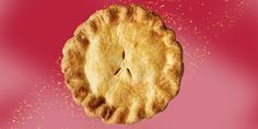 an apple pie on a pink background with gold sprinkles in the air