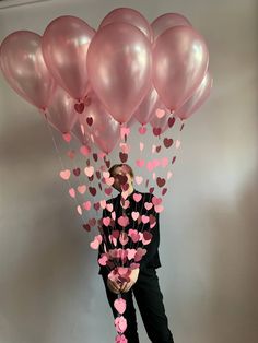 a woman holding pink heart shaped balloons in her hands and standing next to the wall