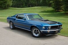 a blue mustang sitting on the side of a road next to a lush green field