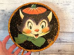 a hand holding up a black and orange plate with an image of a cat on it