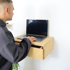 a man standing in front of a desk with a laptop computer on top of it