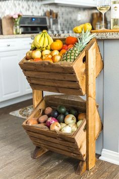 a wooden cart filled with lots of fruit on top of a hard wood floor next to a kitchen counter