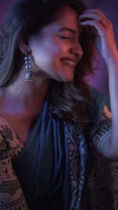 a woman smiling and holding her head in her hands while she wears earrings on top of her head