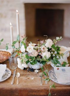 a table topped with flowers and candles next to a plate filled with bread on top of it