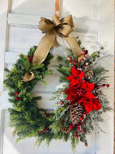 a christmas wreath hanging on a door with red poinsettis and pine cones