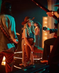 a woman wearing a cowboy hat standing on a stage with other people in the background