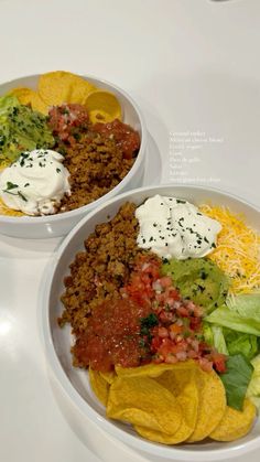 two white bowls filled with taco salad and tortilla chips on top of a table