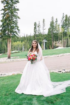 a woman in a wedding dress holding a bouquet and posing for a photo on the grass