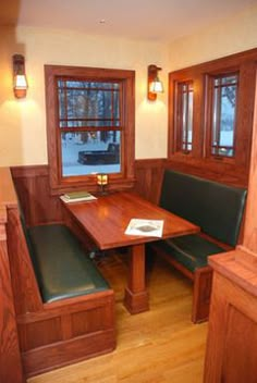 a wooden table sitting in the corner of a room next to two green benches and windows