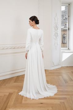 The modest wedding dress with sleeves combines timeless elegance and minimalist design, featuring a sleek, fitted bodice and a flowing A-line skirt that flatters all body types. Made from soft, structured chiffon, it drapes beautifully, with long, romantic sleeves and delicate lace cuffs. The modern boat neckline adds sophistication, while the subtle lace details provide a classic touch. Perfect for any ceremony, this dress offers effortless elegance and comfort with a light, graceful train that Modest A Line Wedding Dress, Modest Long Sleeve Wedding Dress, Modest Long Sleeve Wedding Dresses, Weddind Dress, Romantic Sleeves, Modest Wedding Dresses With Sleeves, Wedding Dress With Sleeves, Wedding Dress With Lace, Modest Wedding Dress