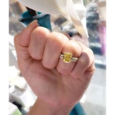 a person holding up a yellow diamond ring in their right hand with the other hand