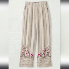 a pair of pants with embroidered flowers on the bottom and side, hanging against a white wall