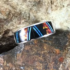 This beautiful Sterling Silver Ring, as part of the Red Moon Collection, features Black Jade, Kingman Turquoise and Blue, Green & Red Lab Opal in a Fancy Inlay Pattern. Dimensions: Ring Width 3/8"; Shank Width 1/8" The ring is designed by David Rosales, one of the finest contemporary Southwest Artists in the world. He is the founder and co-owner of Supersmiths, Inc. of Gallup, NM. Each ring is custom made and carries a lifetime guarantee. Artisan Red Inlay Jewelry, Artisan Red Jewelry With Inlay, Multicolor Fusion Jewelry With Accent Stones, Multicolor Fusion Style Jewelry With Accent Stones, Unique Multicolor Rings With Polished Finish, Red Sterling Silver Jewelry With Inlay, Red Inlay Ring, Multicolor Polished Finish Ring Jewelry, Multicolor Polished Ring Jewelry