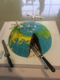 the cake is shaped like an airplane on top of the world map with two knives