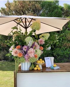 a table with flowers and fruit under an umbrella