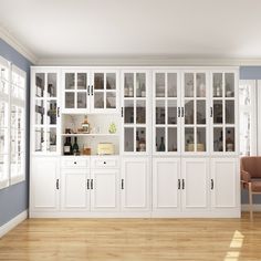 an empty room with white cabinets and wood floors is pictured in this image, there are two chairs on the far side of the room