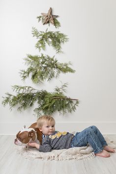 a little boy laying on the floor next to a christmas tree with a dog in his lap