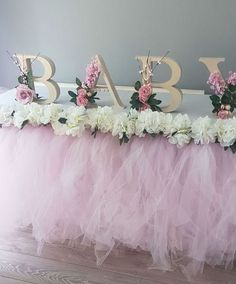 there is a pink tulle table with flowers on it and the letters baby spelled out