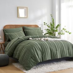 a bed with green comforter and pillows in a room next to a plant on the floor