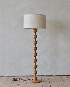 a wooden floor lamp with a white shade on the base and a cord attached to it