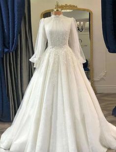 a white wedding dress on display in front of a blue drapeed curtain and mirror