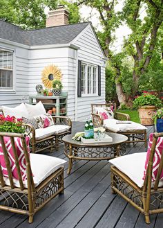 an outdoor patio with chairs, tables and potted plants on the back deck in front of a white house