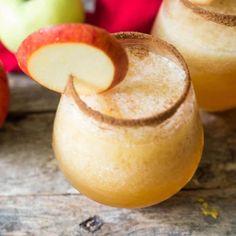 two glasses filled with apple cider next to apples