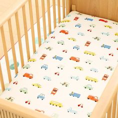 a crib bed with a white sheet with cars and trucks printed on the sheets