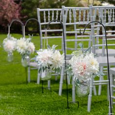 rows of white chairs with flower vases on them in front of an outdoor ceremony