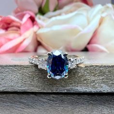 a blue and white diamond ring sitting on top of a wooden table next to flowers