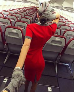 a woman in a red dress and gloves on an airplane looking down at the seats