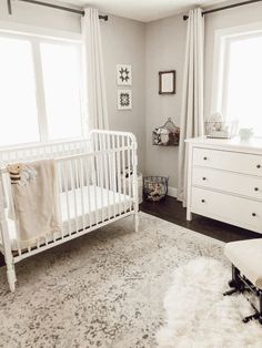 a baby's room with a white crib, dresser and large window in it