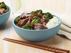 two bowls filled with beef and broccoli next to chopsticks on a table