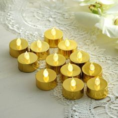 small gold candles are lined up on a lace tablecloth with white flowers in the background