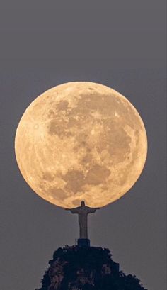 the full moon rising over a statue on top of a hill