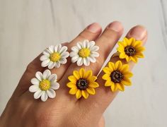 four yellow and white flowers are placed on someone's hand with their fingers in the air