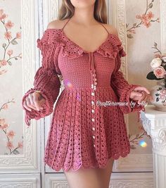 a woman wearing a pink crochet dress with long sleeves and an open shoulder